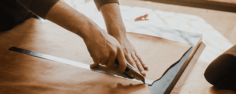 Man hands cutting a piece of brown paper with a utility knife