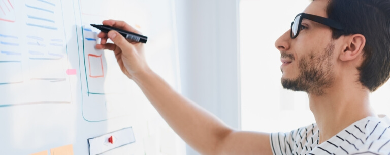 Male app developer outlines code on whiteboard