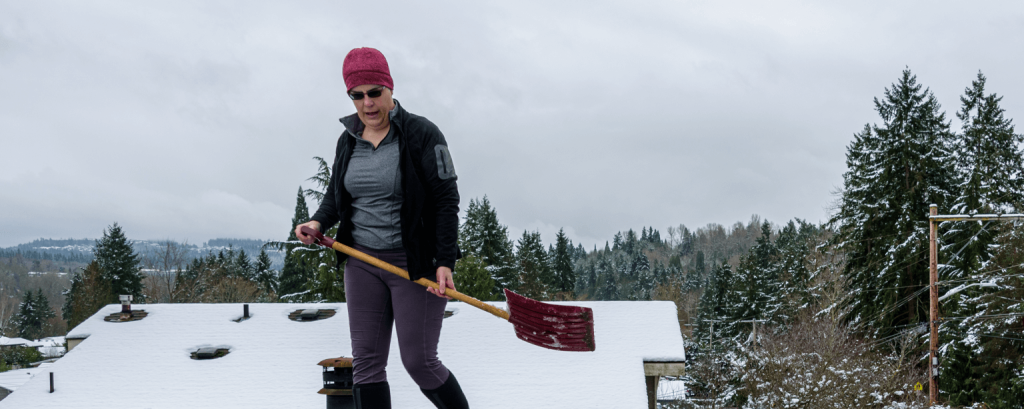 Woman shovelling snow off of a roof