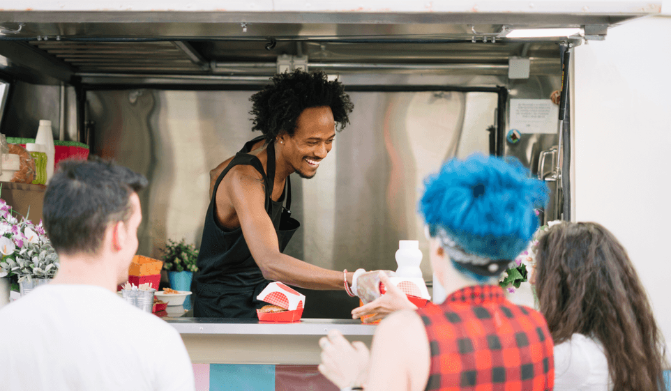 A food truck owner serves food to a customer.