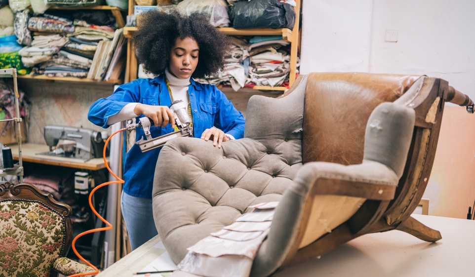 Woman wearing blue shirt while upholstering a chair.