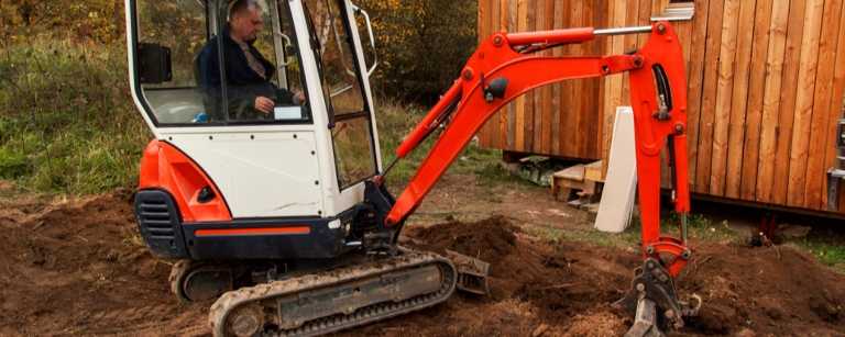Male excavator pilots machinery in yard
