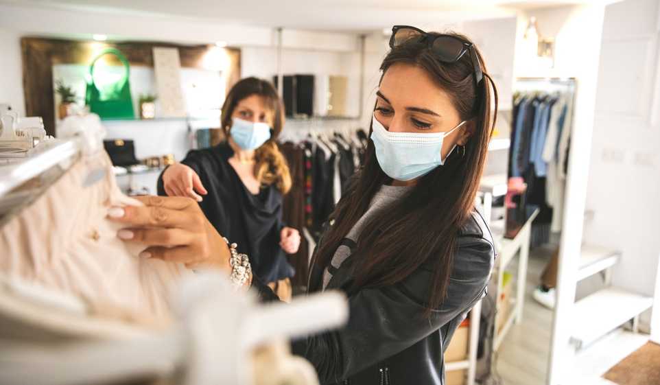 Two women wearing face masks shop in a small business retail store.