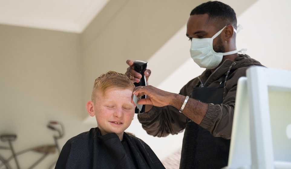 Man wearing a mask while barbering a young boy's hair.