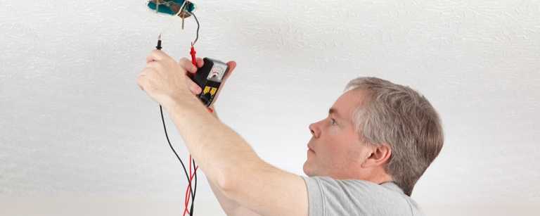 Electrician using meter to test ceiling outlet