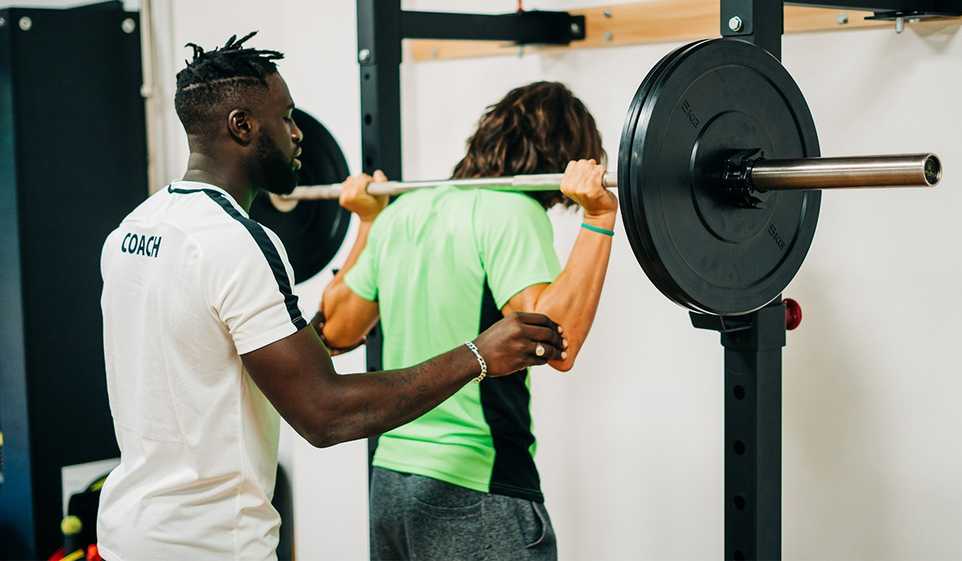 A personal trainer is spotting his male client lifting weights in the gym