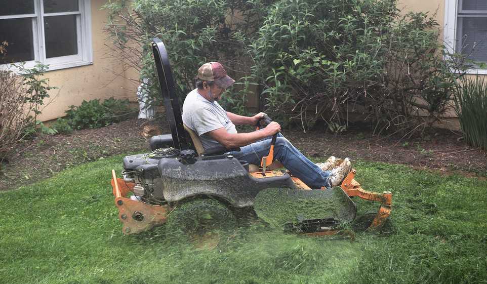 Man riding lawn mower in jeans and white t-shirt with baseball cap