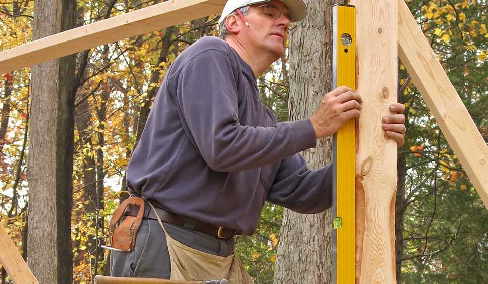 Vermont contractor in grey sweatshirt using a level on a vertical piece of untreated wood