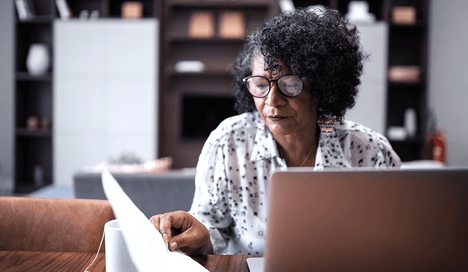 Woman looking at tax forms while sitting in front of a laptop.
