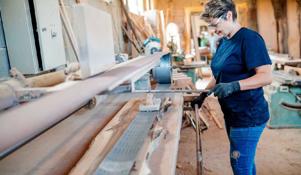 A woman works on a machine in a carpentry shop.