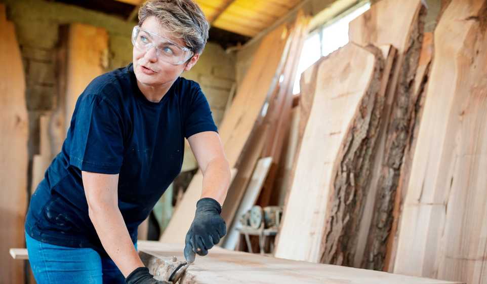 Woman with short blonde hair wearing goggles and woodworking.