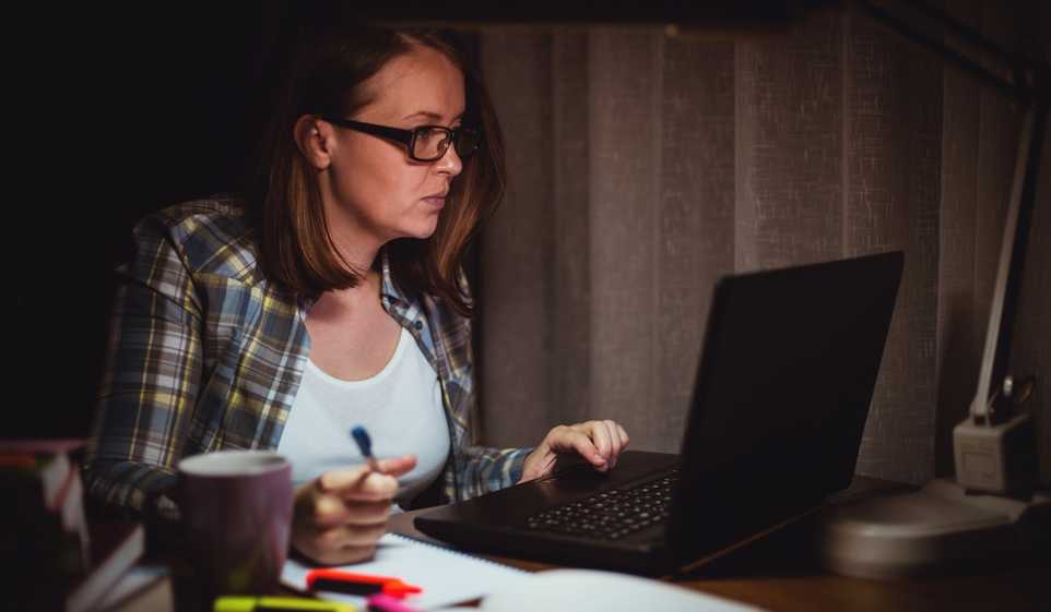 Woman in plaid shirt with glasses sits at computer