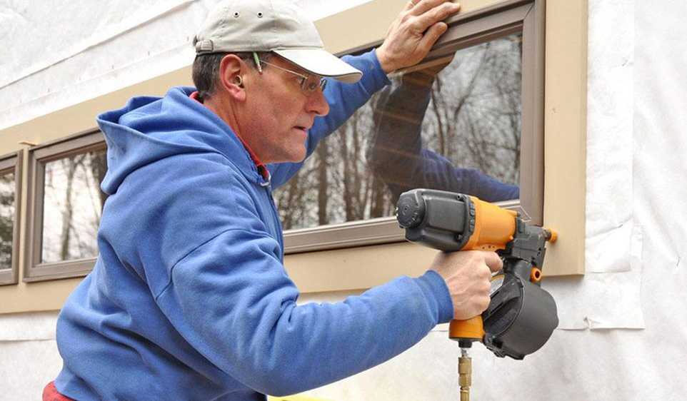 A man who has his general contractor license in Connecticut is using a drill to install new windows on a building