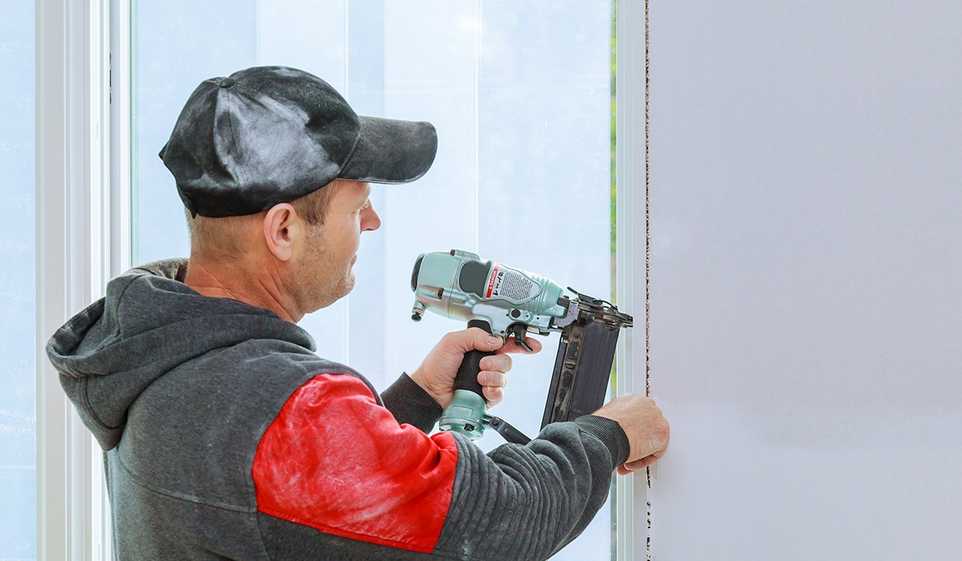 A man in grey and red clothing with a PA contractor license using a drill on a window pane