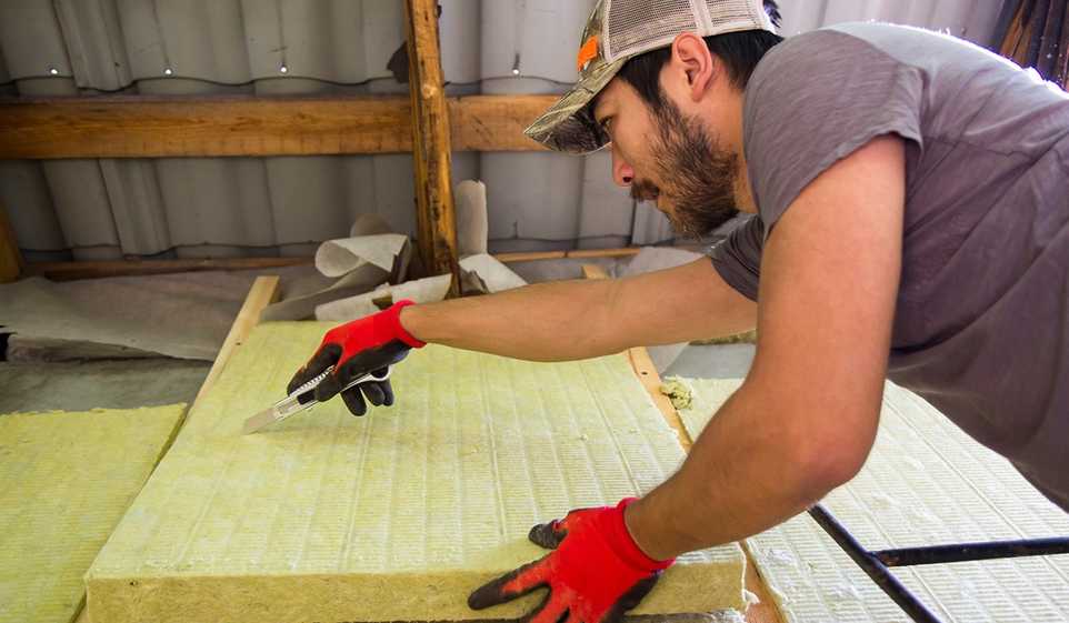 Contractor in baseball cap using a box cutter to cut insulation