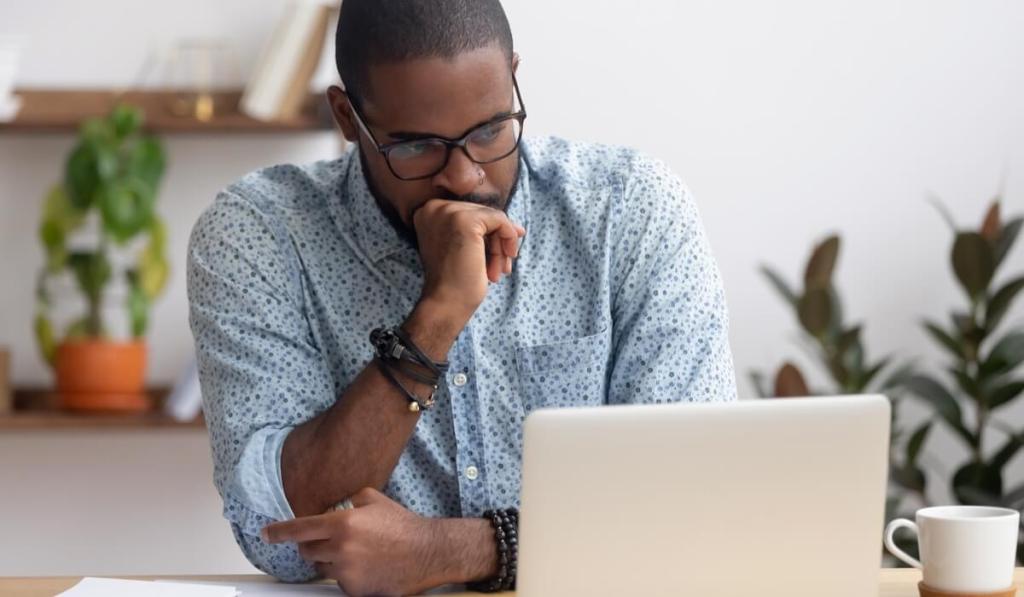 Man with glasses and blue button down shirt looking at his laptop.