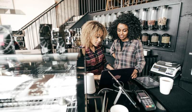 Two women wearing plaid shirts looking at a computer.