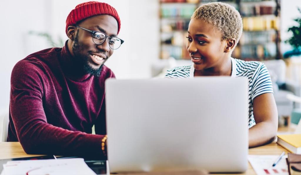 Two people seated next to each other, smiling, looking at laptop,