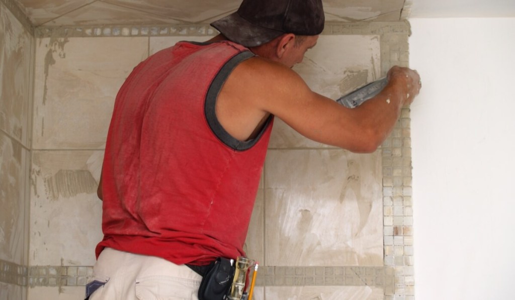 A contractor with a Texas business license works on re-tiling a client's wall.