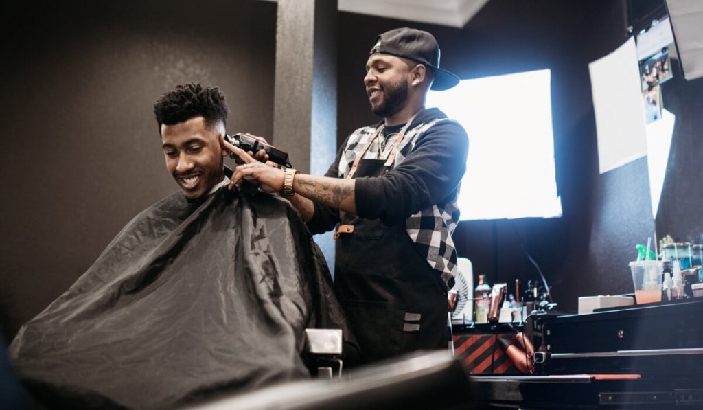 A barber uses a clipper to give a new customer a buzzcut in his barbershop.