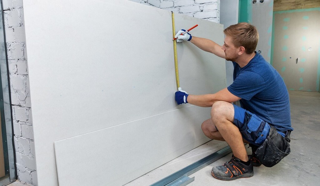 Tennessee contractor using a measuring tape on white sheet rock and marking with a red pencil