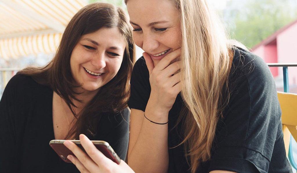 Two women are laughing while looking at these funny landscaping company names