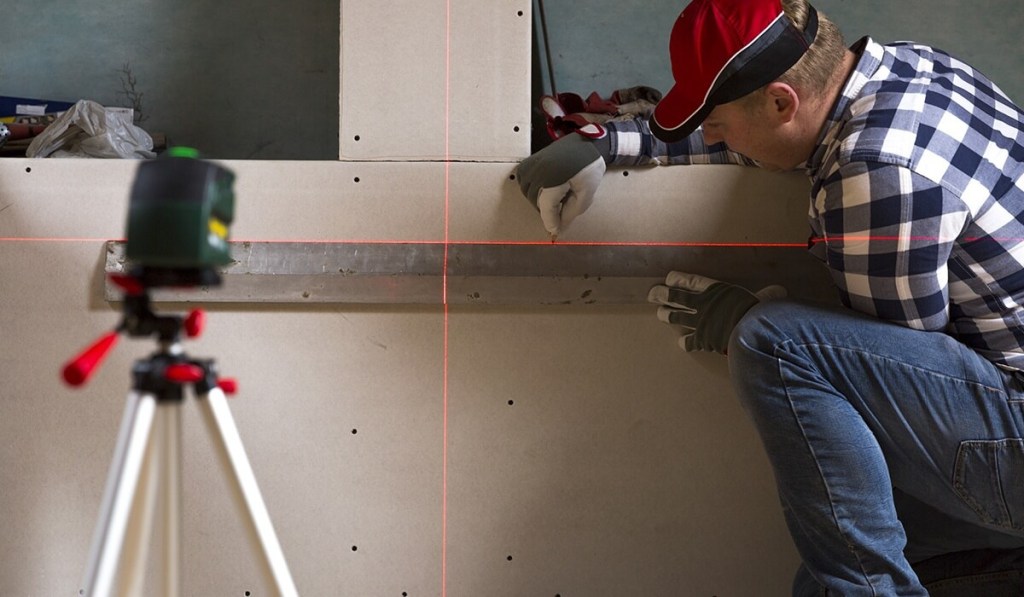 A contractor who owns a contractor’s license in Massachusetts is using a level against a wall to measure placement