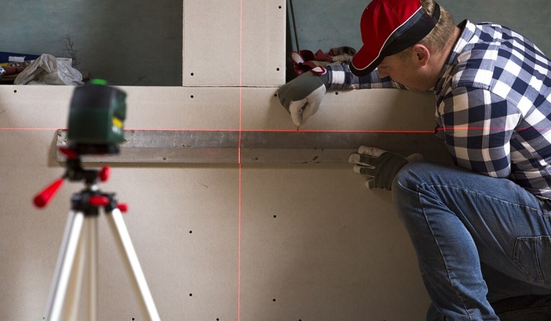 A contractor who owns a contractor’s license in Massachusetts is using a level against a wall to measure placement