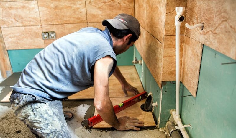 Man measuring plywood on a floor with a red level