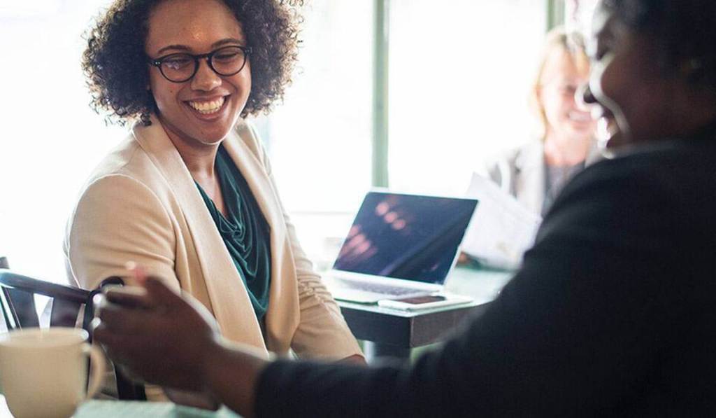 Woman is smiling at another woman's cell phone while learning about word of mouth marketing