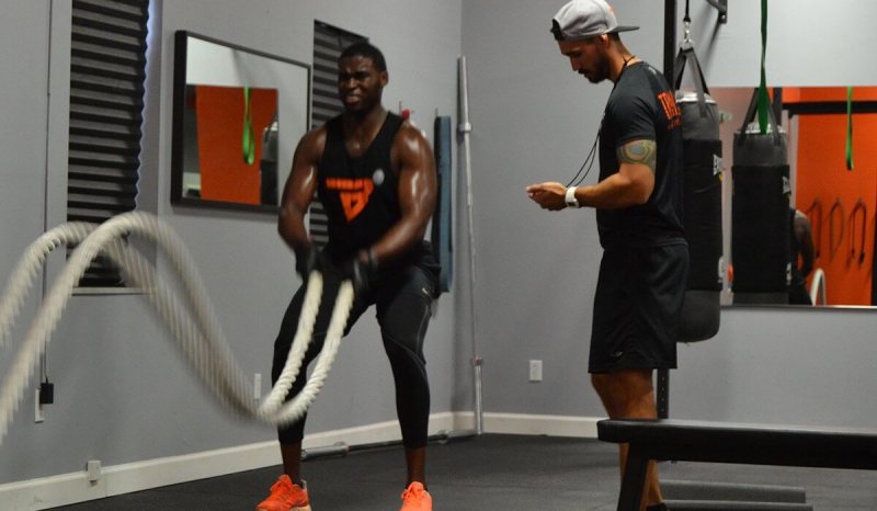 A personal trainer is keeping track of time while his male client is exercising