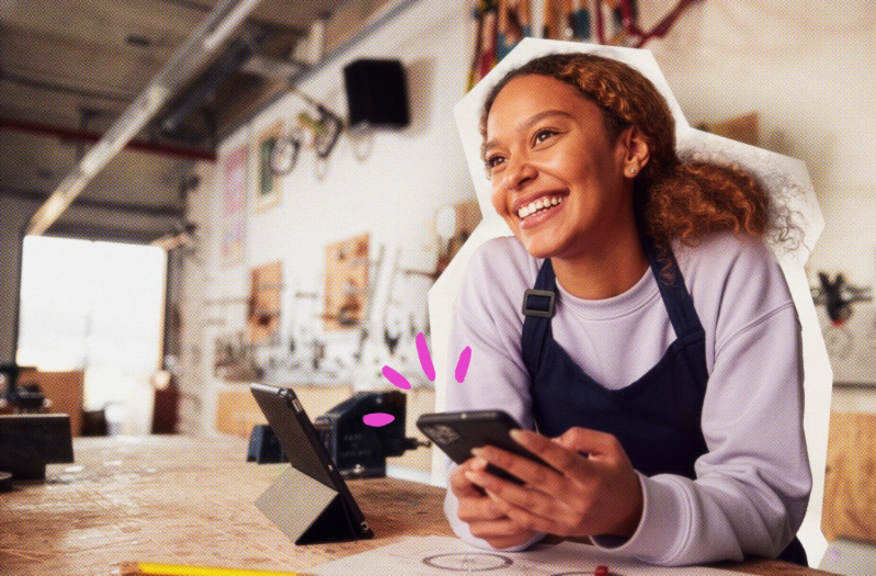 female presenting solopreneur with apronat work counter with card reader holding phone smiling